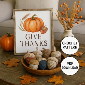 May include: A framed sign with a pumpkin illustration and the words "GIVE THANKS". A wooden bowl contains several crocheted acorns in various colours. A pumpkin and autumn leaves complete the autumnal theme.