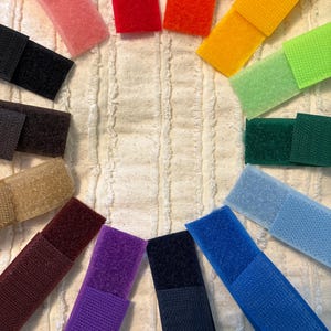 May include: A collection of colorful hook and loop fastener strips in various shades, including pink, red, orange, yellow, green, blue, purple, brown, and black. The strips are arranged in a circular pattern, showcasing their diverse color palette and texture.