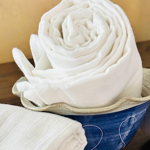 May include: A white cotton dish towel rolled up and placed in a blue and white ceramic bowl. The bowl has a scalloped rim.