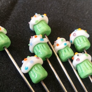 May include: Seven green and white cupcake shaped glass beads with colorful sprinkles on a silver wire.