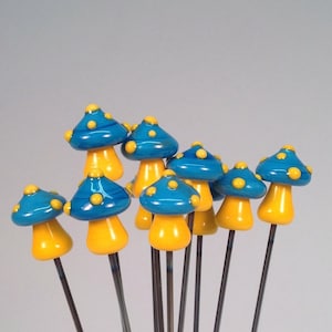 May include: A group of ten blue and yellow glass mushroom shaped beads on metal wires. The mushrooms have yellow dots on the blue tops.