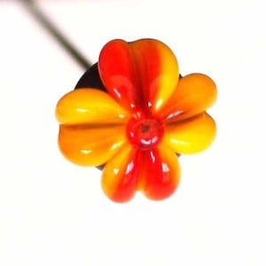 May include: A close-up of a glass flower with five petals. The petals are a gradient of orange and red.