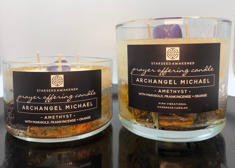 May include: Two glass prayer offering candles labeled "Archangel Michael" with amethyst, marigold, frankincense, and orange. The candles have a black label with white text and gold glitter around the top.