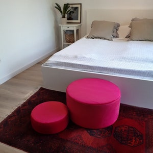 May include: Two bright pink round poufs on a red patterned rug in a bedroom setting.