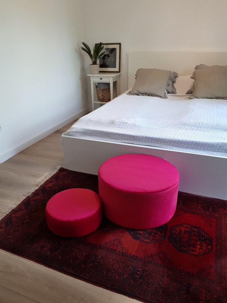 May include: Two bright pink round poufs on a red patterned rug in a bedroom setting.