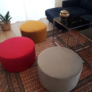 May include: Three round, fabric-covered ottomans in a living room setting. The ottomans are mustard yellow, red, and gray. The ottomans are on a patterned rug.