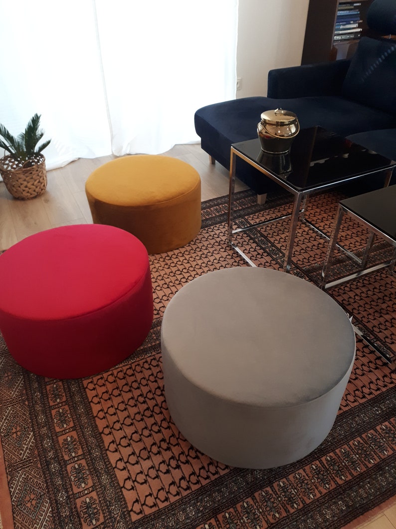 May include: Three round, fabric-covered ottomans in a living room setting. The ottomans are mustard yellow, red, and gray. The ottomans are on a patterned rug.
