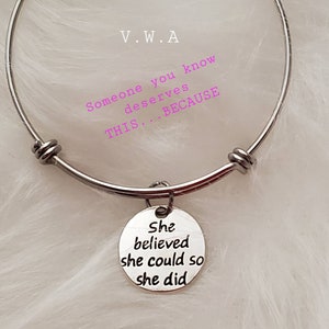 May include: A silver-colored bangle bracelet with a round charm. The charm is engraved with the words "She believed she could so she did." The bracelet also has the text "Someone you know deserves THIS... BECAUSE."