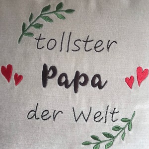 May include: A white pillow with green embroidered leaves and red hearts around the text "tollster Papa der Welt".