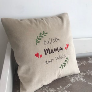 May include: Beige pillow with embroidered green leaves and red hearts. The text "tollste Mama der Welt" is embroidered on the pillow.