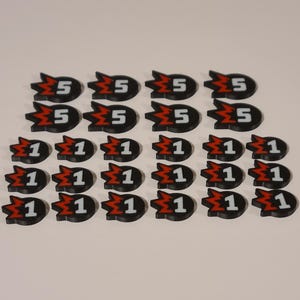 Peut inclure: Un ensemble de 20 jetons de jeu en plastique noir et rouge avec des chiffres blancs. Les jetons présentent un graphique d'explosion stylisé. Il y a huit jetons avec le chiffre "5" et douze jetons avec le chiffre "1".