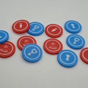 Puede incluir: Un conjunto de fichas de juego circulares rojas y azules. Cada ficha presenta un icono blanco, incluyendo una llave, una flecha hacia arriba y una persona. Las fichas están dispuestas sobre una superficie blanca.