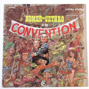 May include: A vintage vinyl record album cover featuring a cartoon illustration of a band called "Homer and Jethro" performing at a convention. The cover is in a bright, colorful style with a red banner that reads "at the Convention".