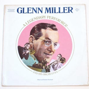 May include: Vintage Glenn Miller album cover featuring a portrait of the musician in a pink circle. The album title is in blue, with the text "A Legendary Performer" and "And His Orchestra". The cover includes illustrations of musicians.