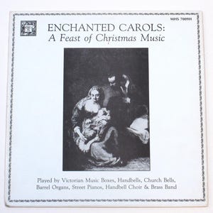 May include: A vintage album cover titled "ENCHANTED CAROLS: A Feast of Christmas Music." The cover features a black and white illustration of a family. The text below indicates the music is played by various instruments, including handbells and barrel organs.