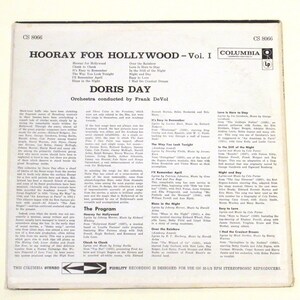 May include: A vintage vinyl record cover for "Hooray for Hollywood - Vol. I" by Doris Day. The cover features a photo of Doris Day in a black and white dress, holding a microphone. The album cover is in a light blue and white colour scheme, with the title of the album in large, bold letters. The album cover also includes a list of songs on the album, including "It's Easy to Remember", "The Way You Look Tonight", and "Over the Rainbow".