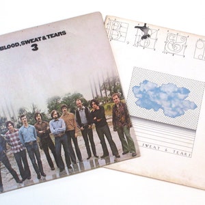 May include: A vintage vinyl record album cover for Blood, Sweat & Tears 3. The front cover features a group of men standing in a field. The back cover features a geometric design with a cloud and the text "Sweat & Tears".