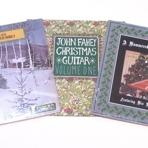 May include: Three Christmas music albums. The first album features a winter scene with a person carrying a Christmas tree. The album title is "Christmas Harmonica-Dobro". The second album features a green and gold floral design and the album title is "John Fahey Christmas *Guitar* Volume One". The third album features a photo of a person playing a hammered dulcimer. The album title is "A Hammered Dulcimer Christmas featuring His Hammered Dulcimer".