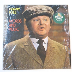 May include: A vintage vinyl record album featuring Benny Hill. The album cover shows a portrait of Benny Hill wearing a tweed cap and suit. The album title "Words and Music" is displayed in yellow and red text. A "Capitol Value" sticker is on the cover.