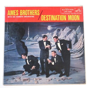 May include: Vintage vinyl record album cover for "Destination Moon" by Ames Brothers with Sid Ramin's Orchestra. The cover features four men in tuxedos on a lunar landscape with a rocket ship and the moon in the background. The album title is in yellow text.
