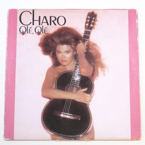 May include: Album cover featuring the name "Charo" in large black letters, with "Olè, Olè" below. A woman with long brown hair holds a black acoustic guitar against a pink background. Pink borders frame the image.