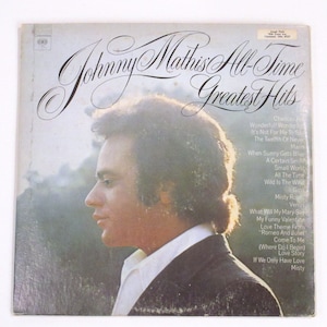 May include: A vintage vinyl record album cover featuring a portrait of Johnny Mathis, a popular American singer. The album title is "Johnny Mathis All-Time Greatest Hits" and lists a selection of his most popular songs.