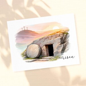 May include: A watercolor painting of a stone tomb with a large, round stone rolled away. The tomb is set against a backdrop of a sunset sky with three crosses on a hill in the distance. The text "HE IS RISEN" is written in cursive below the tomb.