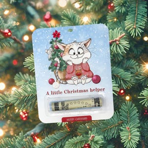 May include: A Christmas card featuring a cartoon cat wearing a red sweater with a reindeer design. The cat is sitting next to a small Christmas tree. The card says "A little Christmas helper" and "Merry Christmas".
