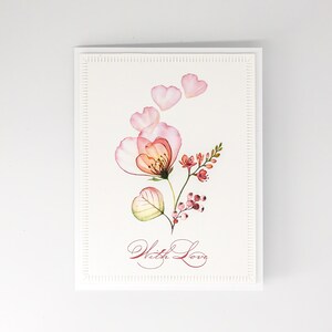 May include: A white greeting card with a watercolor floral design. The illustration features a delicate pink and orange flower with heart-shaped petals and the words "With Love" in cursive script.