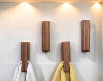 May include: Four wooden towel hooks mounted on a white tiled wall. Two towels are hanging on the hooks.