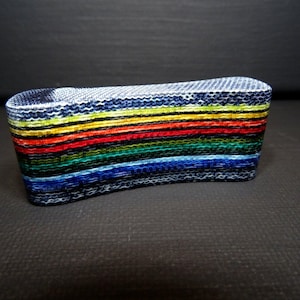May include: A woven, rectangular object with a curved top, showcasing a vibrant spectrum of colors. The layers display a rainbow of hues, including red, orange, yellow, green, blue, and indigo. The edges are a dark blue and white.