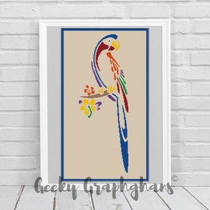 May include: Framed cross-stitch art featuring a colorful parrot perched on a branch with yellow flowers. The parrot has blue, red, orange, and green feathers. The artwork is set against a beige background with a blue border and white frame.