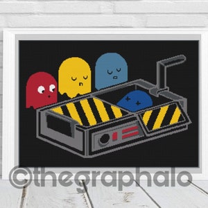 May include: Framed cross-stitch art featuring a black background with pixelated ghosts in red, yellow, and blue. A gray and yellow ghost-catching device is in the center. The artwork is in a white frame.