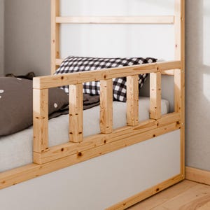 Könnte beinhalten: Ein hölzerner Bettrahmen mit einer hellgrauen Platte und einer natürlichen Holzoberfläche. Das Bett hat ein Sicherheitsgeländer und eine Leiter. Kissen mit einem Punkt- und Karomuster sind auf dem Bett zu sehen.