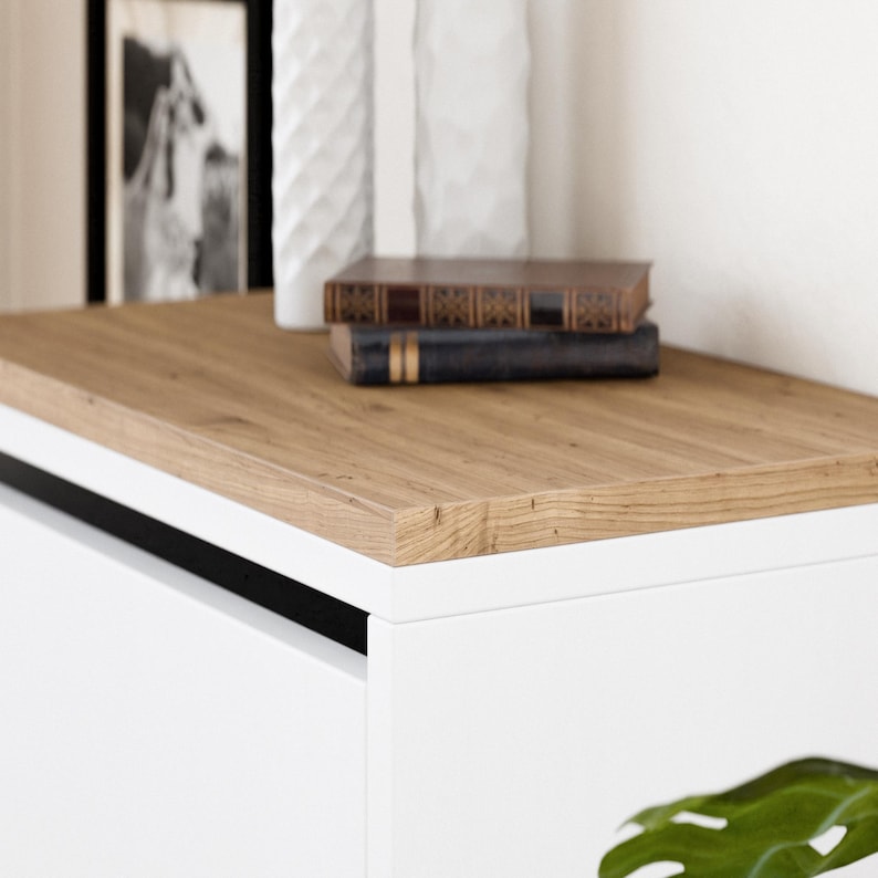 May include: A white cabinet with a wood top and a black trim. The cabinet has a drawer and is sitting on a white surface.