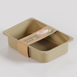 Könnte beinhalten: Eine beige rechteckige Aufbewahrungsbox mit einem braunen Papierband. Das Band trägt den Text "DESIGNED FOR TROFAST" und eine kleine Illustration. Die Box ist leer und hat ein schlichtes, modernes Design.