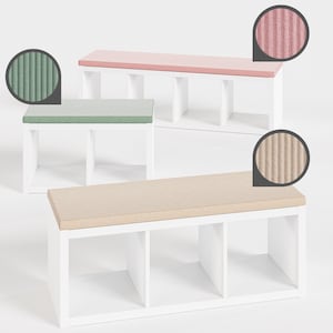 Op de afbeelding: Drie witte opbergbanken met verschillende gekleurde bovenkanten: lichtroze, lichtgroen en lichtbruin. Elke bank heeft een wit frame met drie open compartimenten. De bovenkanten hebben een getextureerd, geribbeld oppervlak.