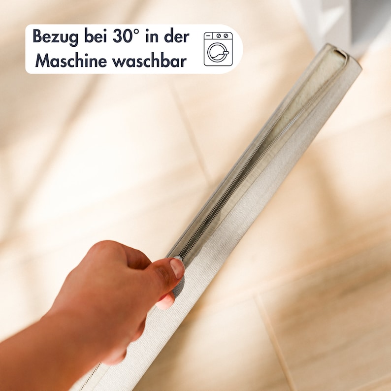 May include: A close-up of a zipper on a light gray fabric cover. The cover has a machine washable label with the text "Bezug bei 30&deg; in der Maschine waschbar" and a washing machine icon.