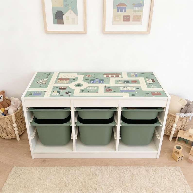 May include: A white rectangular storage unit featuring a top surface printed with a green town map graphic. The unit contains six removable sage green plastic bins arranged in two rows of three, providing organized storage for various items.