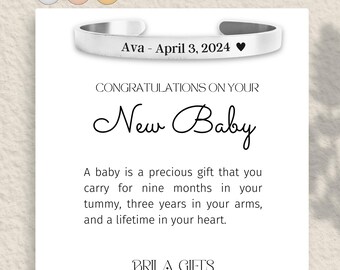 May include: A silver bangle bracelet with the text "Ava - April 3, 2024" and a heart symbol. The bracelet is on a white card with the text "Congratulations on your New Baby" and a message about the precious gift of a baby.