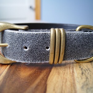 May include: A black leather belt with a brass buckle and a decorative brass accent. The belt is distressed and has a worn look.
