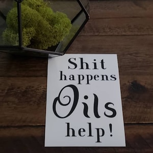 May include: White sign with black text that reads "Shit happens Oils help!"