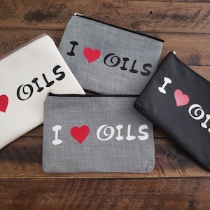 May include: Four zippered pouches with the text "I love oils" printed on them. The pouches are in different colors: white, gray, black, and gray. The text is in black and white with a red heart.