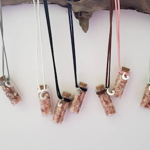 May include: Seven small glass bottles filled with pink Himalayan salt crystals, each with a silver crescent moon charm and a cord for hanging. The bottles are hanging from a branch.