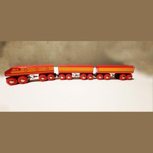 May include: A red wooden toy train with three cars. The engine has a yellow stripe and the cars have yellow squares. The train has black wheels.