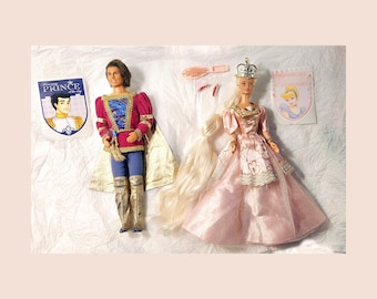 May include: A Barbie doll dressed as a princess in a pink gown with a crown and long blonde hair. A prince doll in a red and blue costume with a cape stands next to her. The dolls are on a white background with a card that says "Happy Birthday".