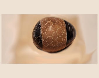 May include: A brown and black egg-shaped stone with a geometric pattern carved into it. The stone is smooth and polished.