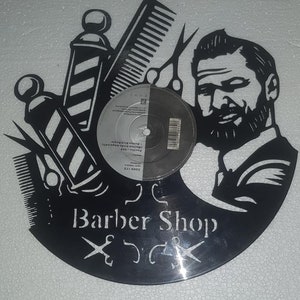 Può includere: Disco in vinile nero con un design a silhouette bianca di un barbiere. Il design include un palo da barbiere, forbici, un pettine e un uomo con la barba. Il testo "Barber Shop" è stampato sul disco.
