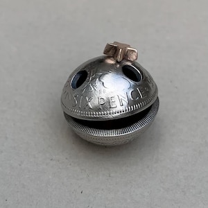 May include: A silver Christmas ornament shaped like a bell, made from two sixpence coins. The top of the bell has a gold star.