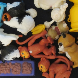 Könnte beinhalten: Eine Sammlung bunter Plastikspielzeugtiere, darunter ein Affe, ein Waschbär, ein Hund und eine Katze. Die Spielzeuge sind auf einer blauen Oberfläche angeordnet.